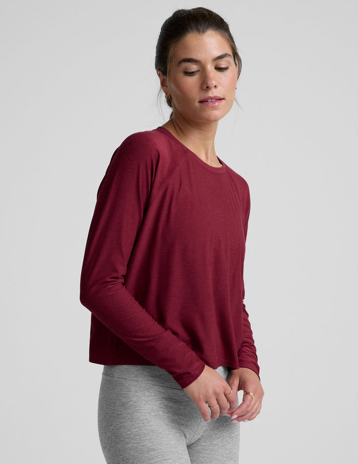 Woman wearing a burgundy long-sleeve top and gray leggings on a light gray background.