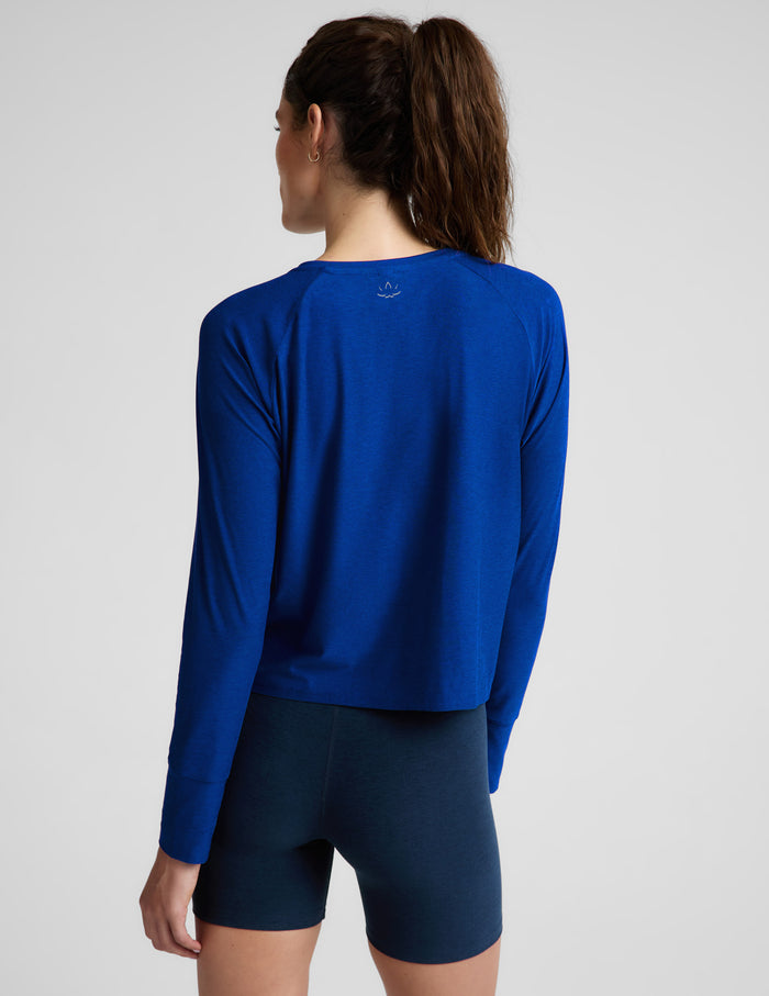 A woman modeling a royal blue long-sleeve athletic top with raglan sleeves and dark navy fitted shorts against a light gray studio background.