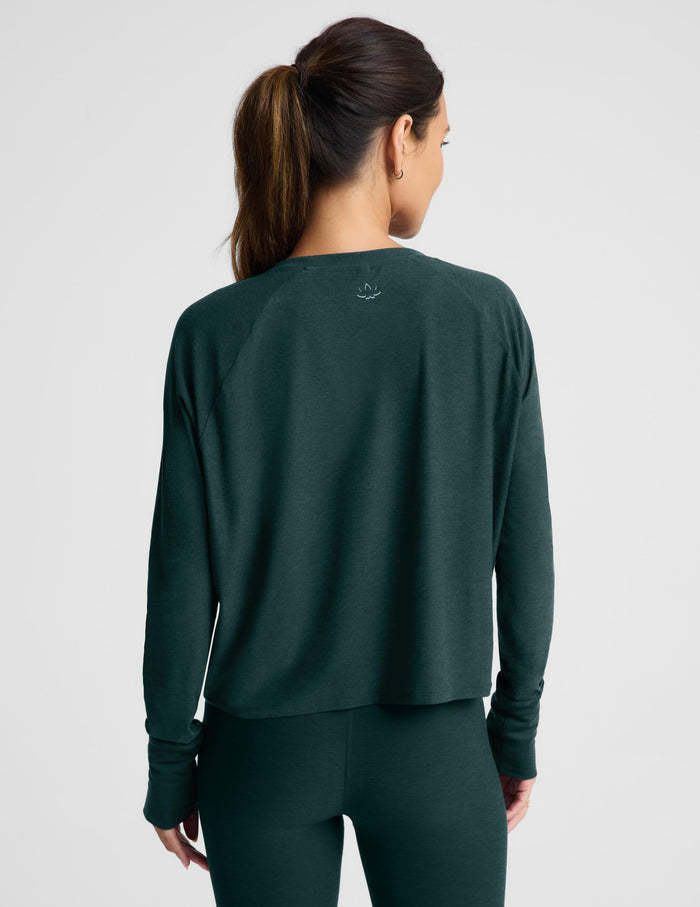A woman modeling a dark forest green long-sleeve cropped top and matching leggings against a light gray studio background.