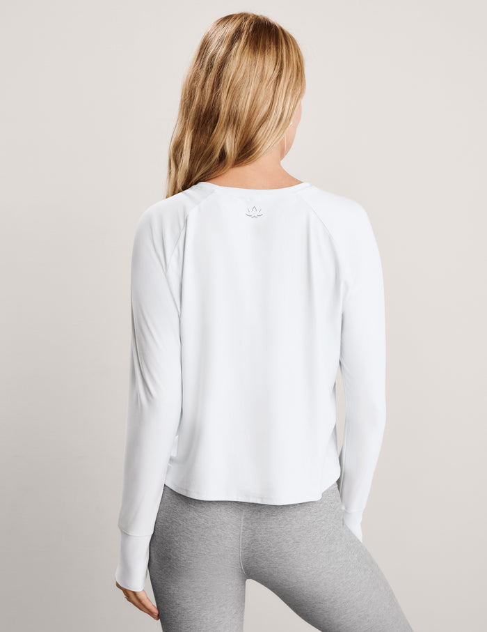 A woman modeling a white long-sleeve crewneck athletic top paired with heather gray leggings, set against a plain light gray studio background.