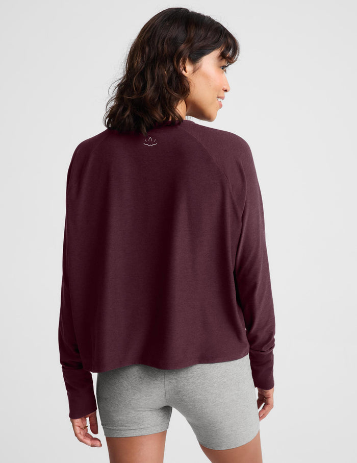 A woman wearing a dark burgundy long-sleeve crewneck top and heather gray bike shorts, standing against a light gray studio background.