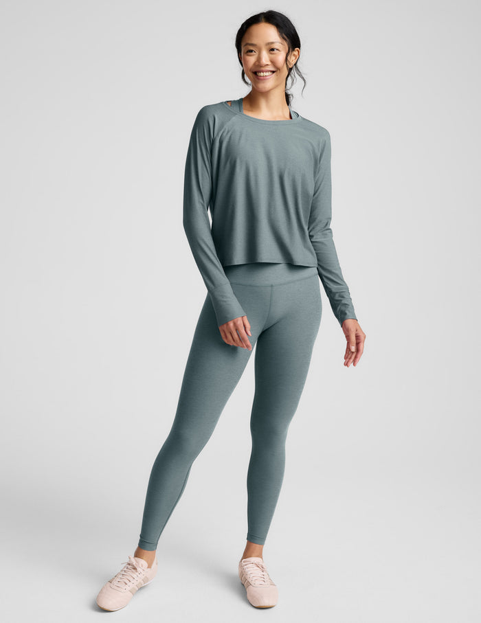 Woman wearing a green long sleeve and leggings against a plain background.