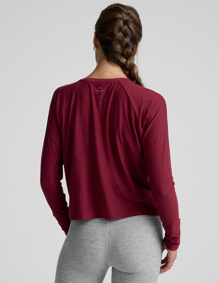 Woman wearing a burgundy long-sleeve top and gray leggings on a light gray background.
