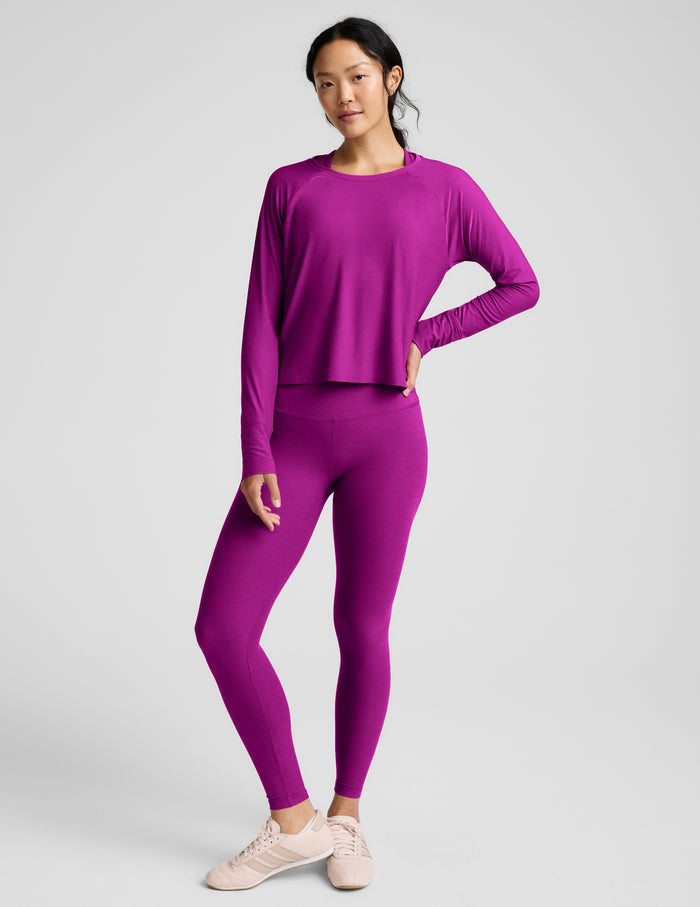 A woman modeling a matching magenta-purple long-sleeve top and leggings set against a solid light gray background.
