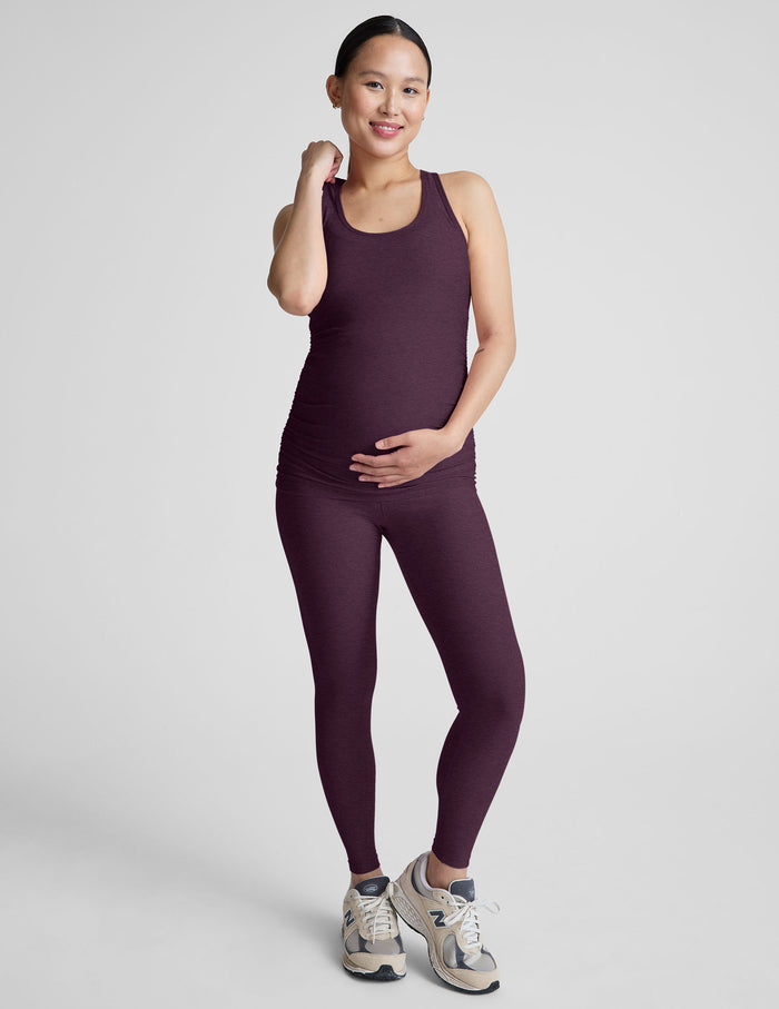 Woman wearing a purple maternity tank top and leggings on a light gray background.