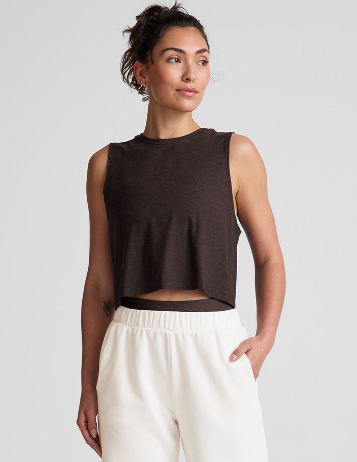 Woman wearing a brown cropped tank top and white sweatpants against a plain background.