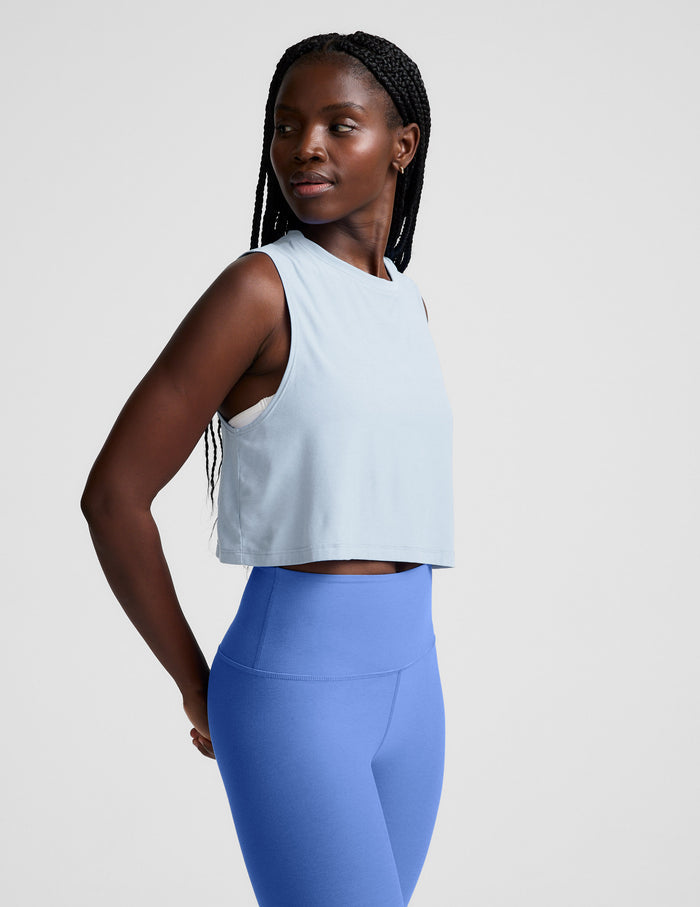 Woman wearing a light blue sleeveless top and blue leggings on a plain background.