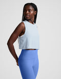 Woman wearing a light blue sleeveless top and blue leggings on a plain background.
