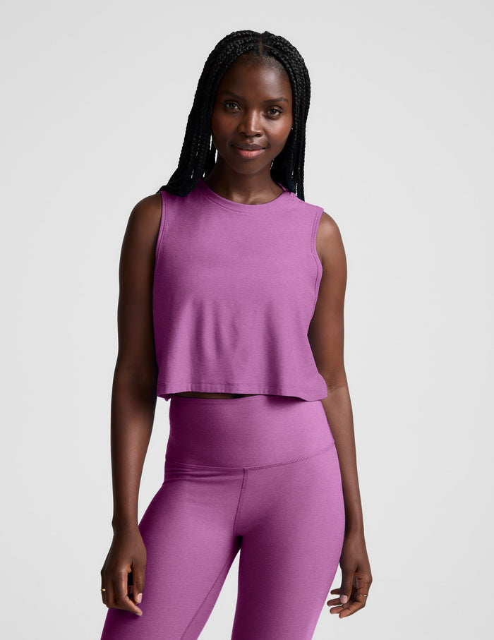 Woman wearing a purple cropped tank and leggings against a plain background.