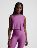 Woman wearing a purple cropped tank and leggings against a plain background.