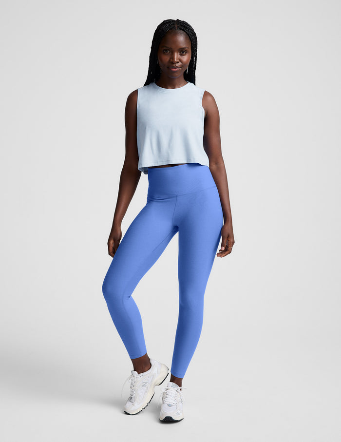 Woman wearing a light blue sleeveless top and blue leggings on a plain background.