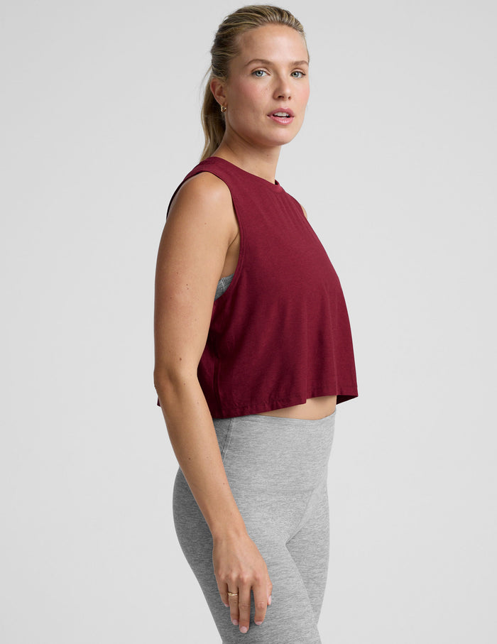 Woman wearing a burgundy sleeveless top and gray leggings on a light gray background.