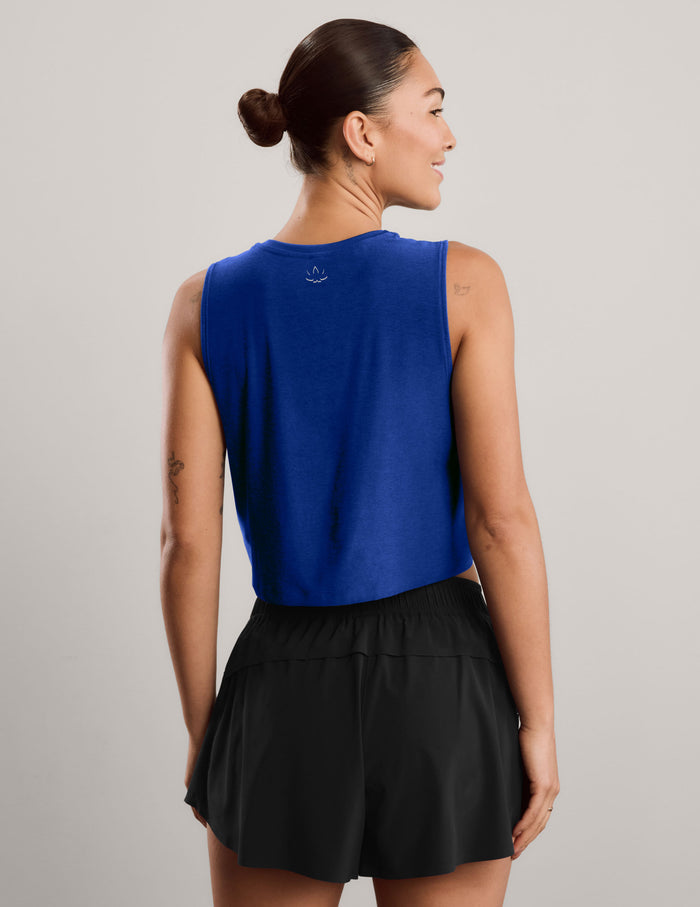 A woman modeling a royal blue sleeveless crop top and black athletic shorts against a light gray studio background.