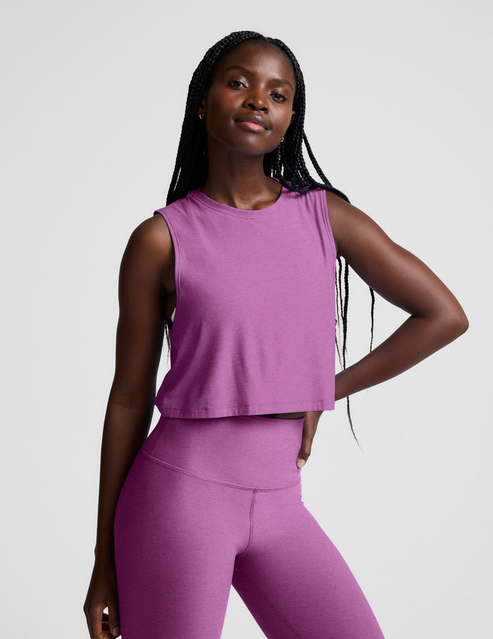 Woman wearing a purple cropped tank and leggings against a plain background.