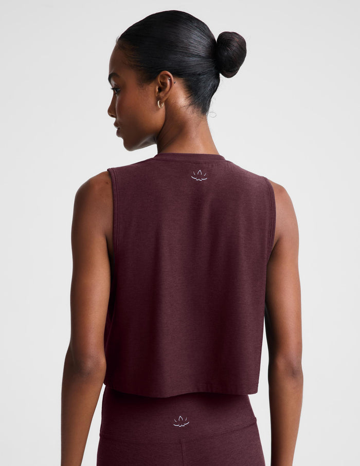 A woman modeling a sleeveless cropped tank top and matching leggings in a deep burgundy color, set against a plain light gray studio background.