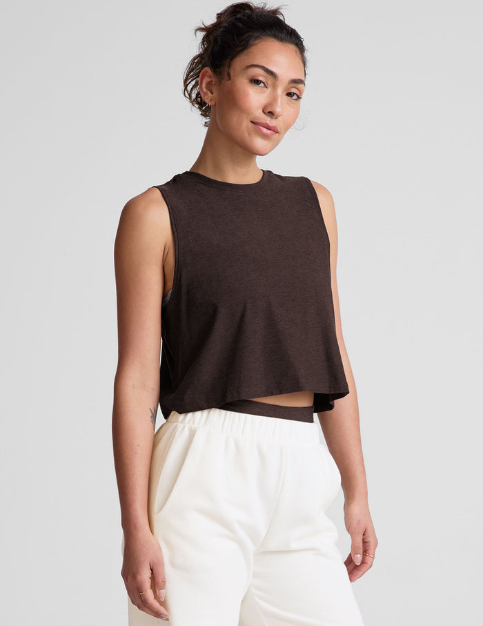 Woman wearing a brown cropped tank top and white sweatpants against a plain background.