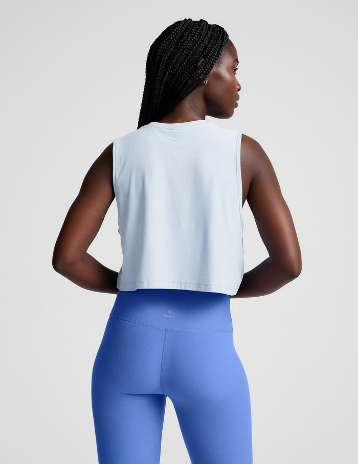 Woman wearing a light blue sleeveless top and blue leggings on a plain background.