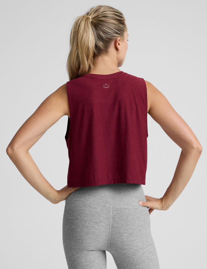Woman wearing a burgundy sleeveless top and gray leggings on a light gray background.