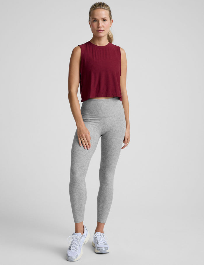 Woman wearing a burgundy sleeveless top and gray leggings on a light gray background.
