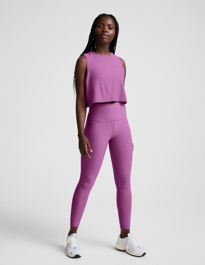 Woman wearing a purple cropped tank and leggings against a plain background.