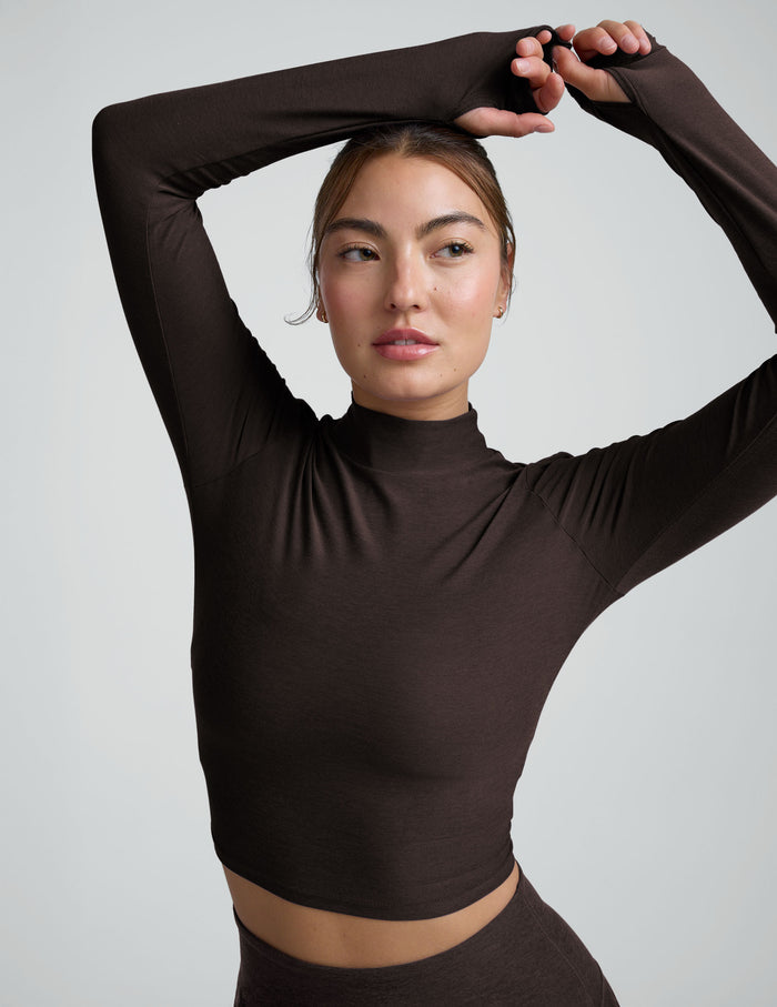 model wearing a brown mock neck cropped long sleeve against a plain background.