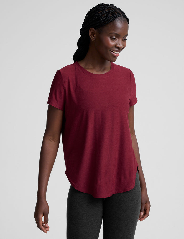 Woman wearing a red t-shirt and black leggings on a light gray background.