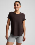 A woman modeling a dark brown short-sleeve crewneck top paired with heather gray bike shorts, photographed against a solid light gray studio background.