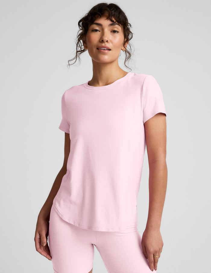 Woman wearing a pink short sleeve top and biker shorts on a light gray background.