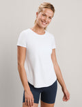 A smiling woman wearing a plain white short-sleeve crewneck top and navy blue fitted shorts, standing against a light gray studio background.