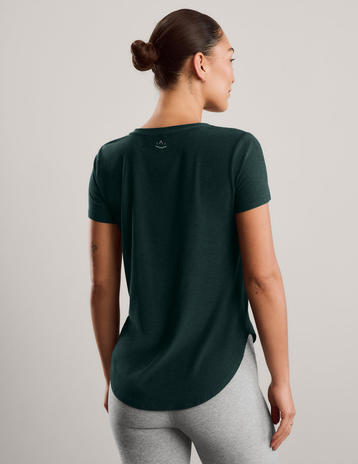 Woman wearing a green short sleeve t-shirt and gray capri leggings against a plain background.