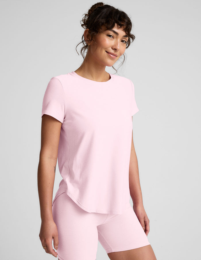 Woman wearing a pink short sleeve top and biker shorts on a light gray background.