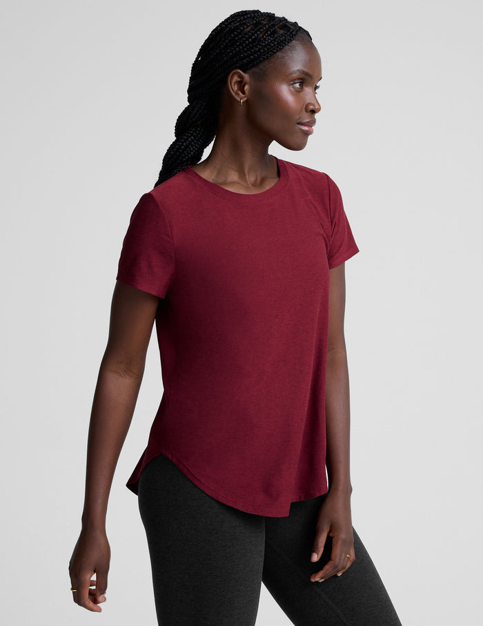 Woman wearing a red t-shirt and black leggings on a light gray background.