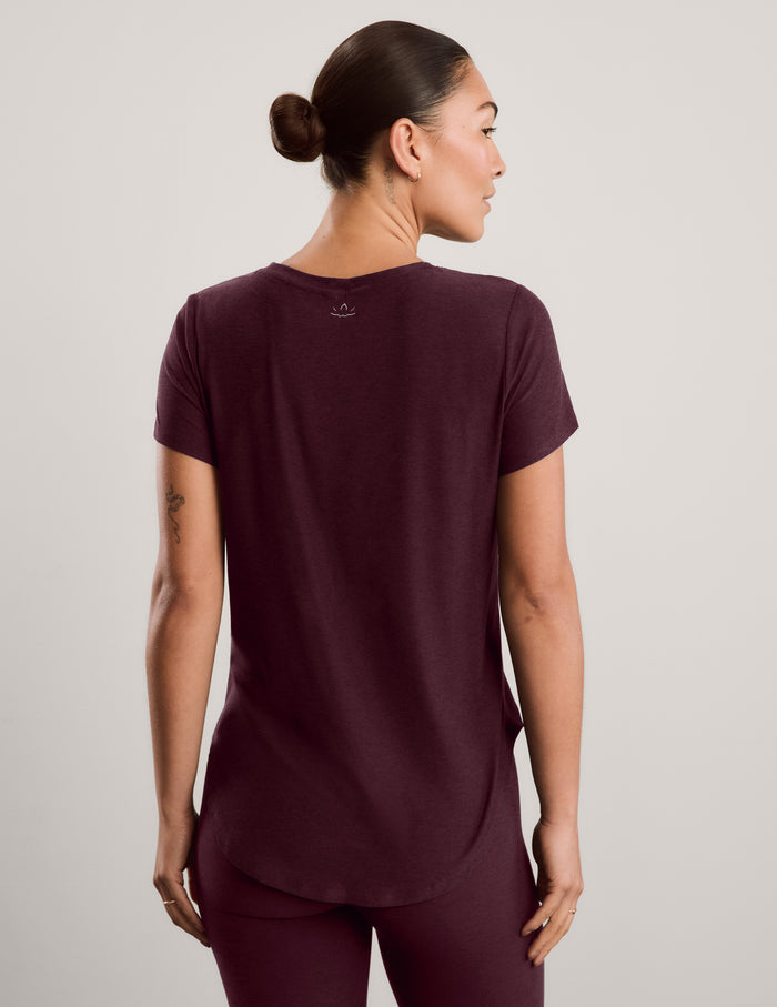 A woman wearing a short sleeve burgundy t-shirt and matching leggings against a plain studio background.