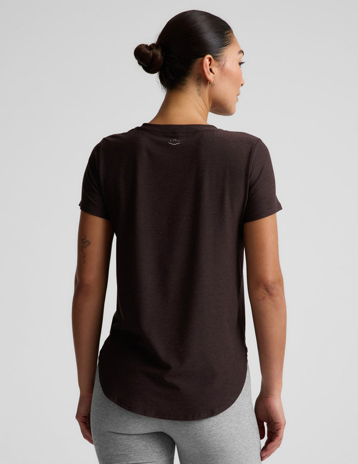 A woman modeling a dark brown short-sleeve crewneck top paired with heather gray bike shorts, photographed against a solid light gray studio background.