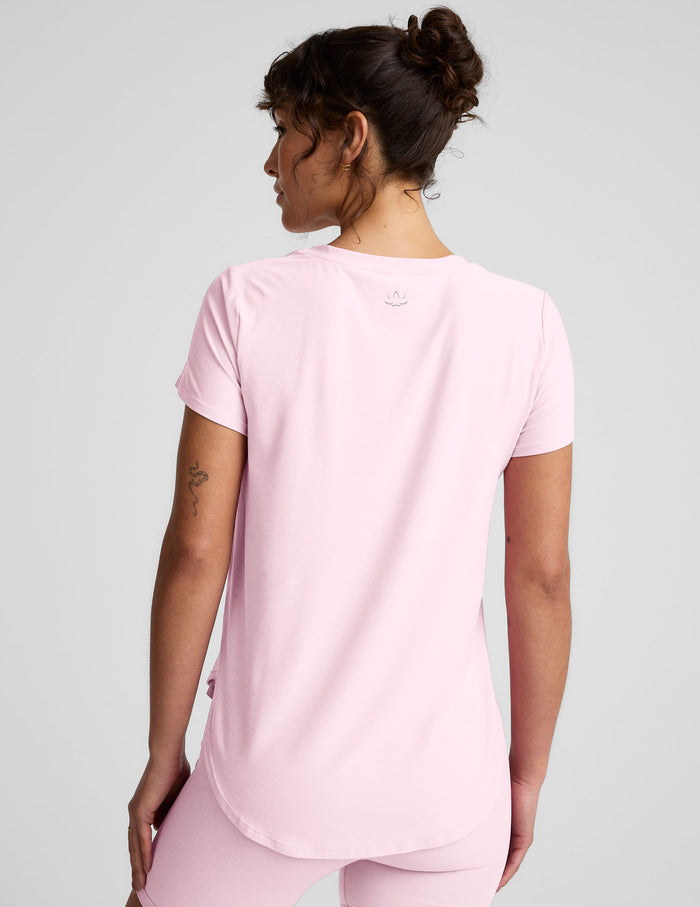 Woman wearing a pink short sleeve top and biker shorts on a light gray background.