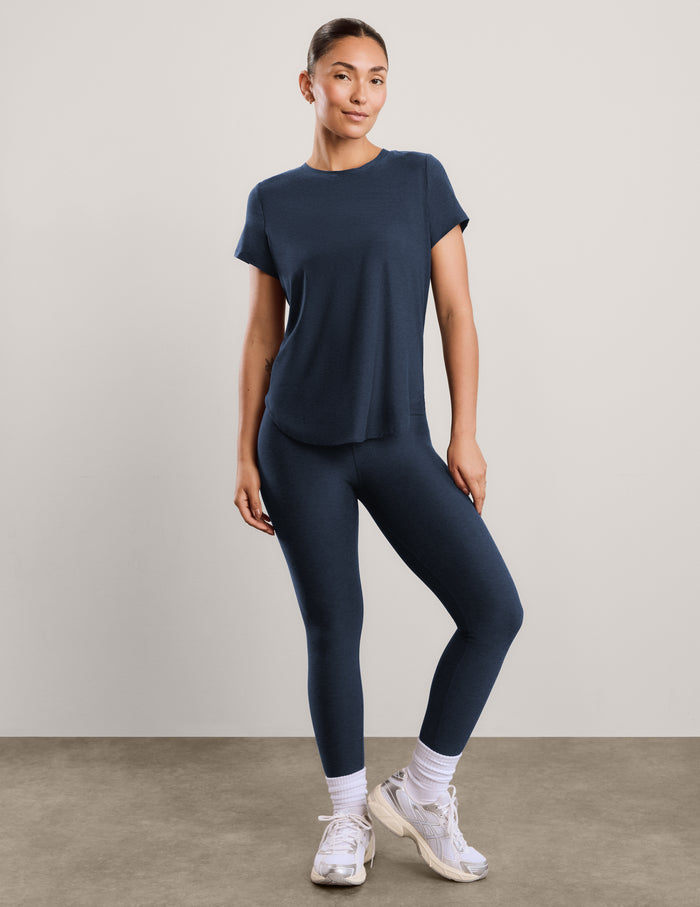 Woman wearing a blue short sleeve t-shirt and leggings against a plain background.