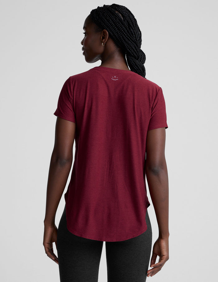 Woman wearing a red t-shirt and black leggings on a light gray background.