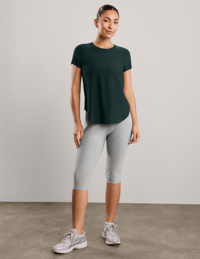 Woman wearing a green short sleeve t-shirt and gray capri leggings against a plain background.