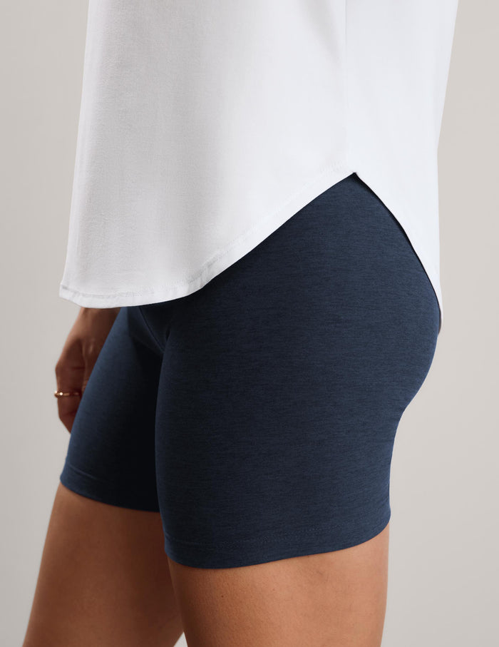 Close-up of a person wearing dark navy heathered biker shorts with a white top, shown from the waist down against a light gray studio background.