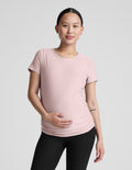 Woman wearing a pink maternity t-shirt and black maternity leggings on a plain background.
