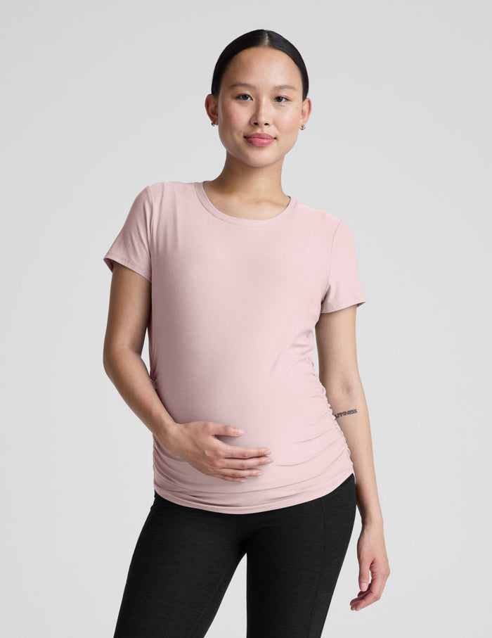 Woman wearing a pink maternity t-shirt and black maternity leggings on a plain background.