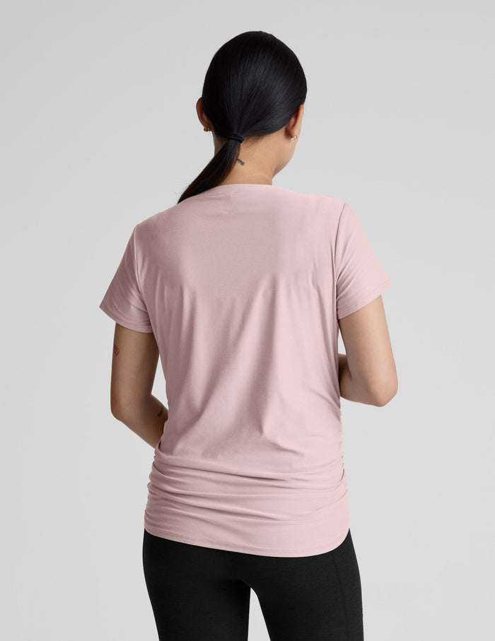 Woman wearing a pink maternity t-shirt and black maternity leggings on a plain background.