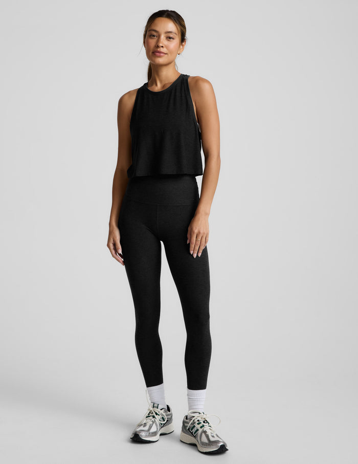 Woman wearing a black sleeveless cropped racerback tank and leggings against a light gray background.