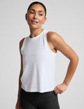 A woman modeling a white sleeveless athletic tank top paired with black biker shorts, photographed against a clean light gray studio background.