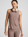 Woman wearing a brown sleeveless top and leggings with white headphones on a light gray background.