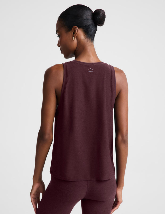 A woman modeling a sleeveless heathered burgundy tank top and matching leggings against a light gray studio background.