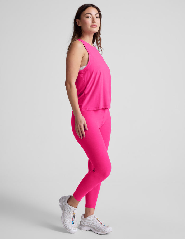 Woman wearing a bright pink sleeveless top and leggings on a light gray background.