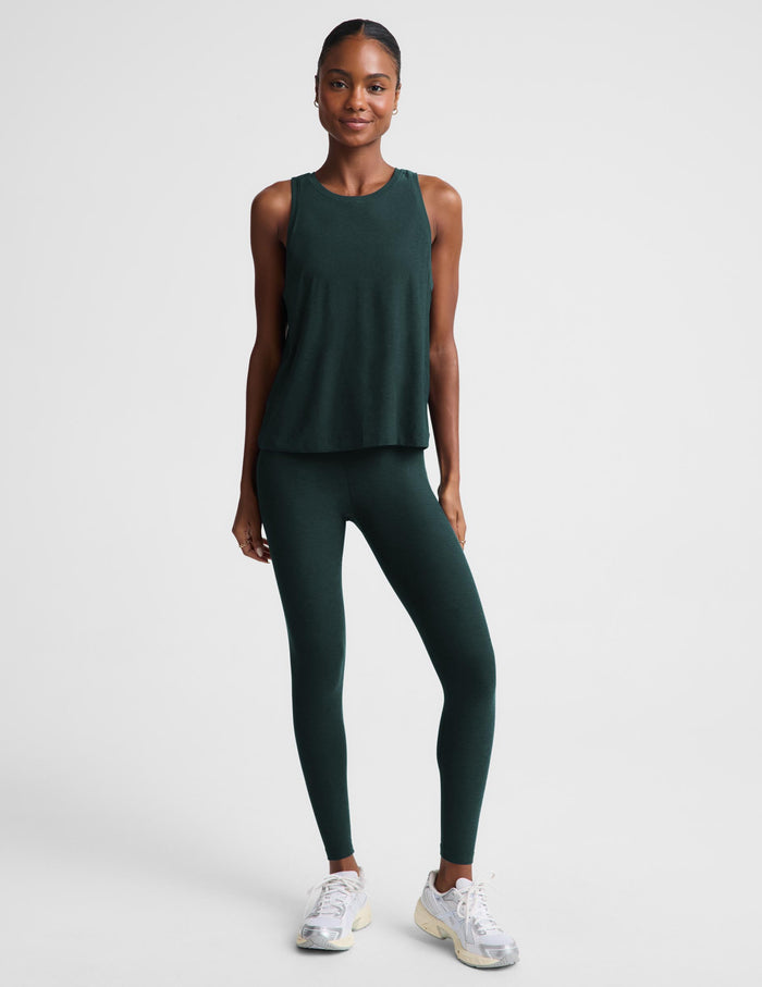 Woman wearing a green tank top and matching leggings against a plain studio background.