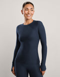 A woman modeling a dark navy blue long-sleeve crewneck top and matching leggings against a plain light gray studio background.