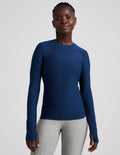 Woman wearing a blue long-sleeve top and gray leggings on a light gray background.